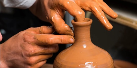 Handen die klei vormen op de draaischijf in het atelier
